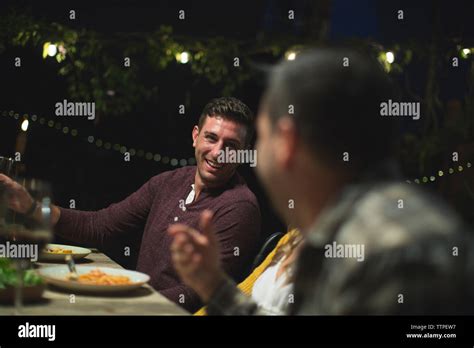 Smiling Friends Talking While Sitting At Table During Dinner Party