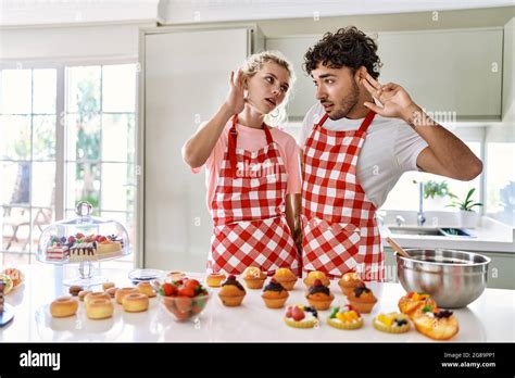 Couple Of Wife And Husband Cooking Pastries At The Kitchen Smiling With Hand Over Ear Listening