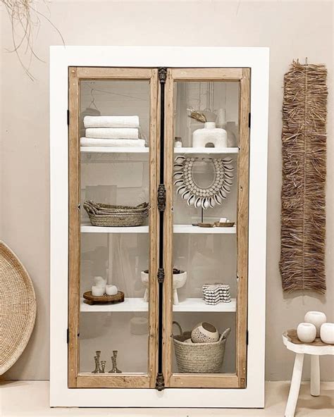 A White Cabinet With Glass Doors And Baskets On The Top Shelf In Front