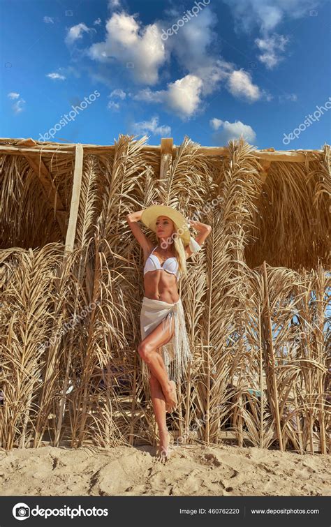 Sexy Woman Wearing Bikini Standing At Lounger Under Straw Canopy At