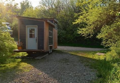 A Tiny House Sits In The Middle Of A Wooded Area With Sun Shining On It