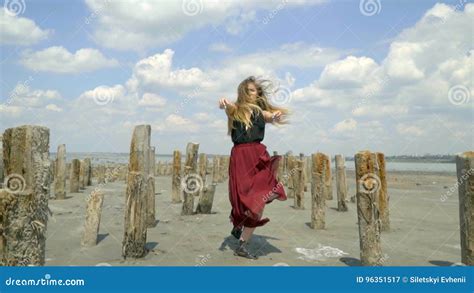 A Beautiful Blonde In A Dress Gently Walks Along The Estuary Amid The