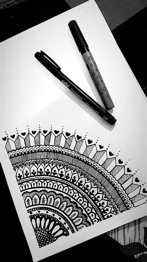 a pen sitting on top of a piece of paper next to a drawing with an intricate design