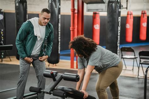 Athletic trainer controlling black woman doing exercises on gym ...