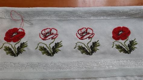 Three Red Flowers Are Embroidered On A White Cloth With Green Leaves