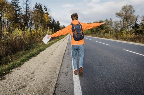 Vista Traseira Do Homem Segurando O Mapa E Caminhando Pela Estrada