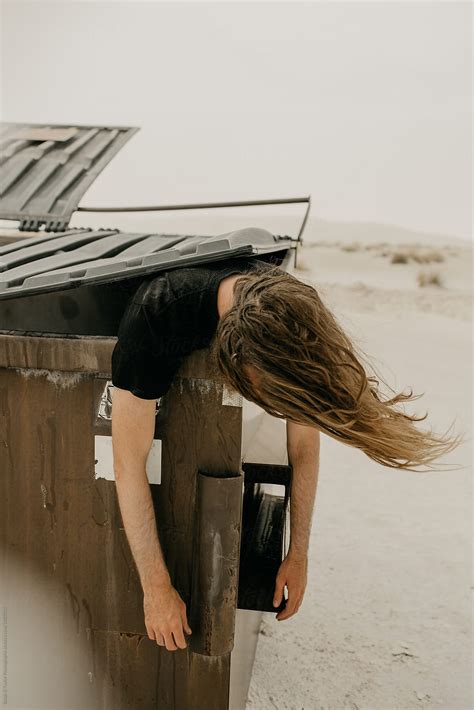 Man Hanging Dead Over A Dirty Trash Bin With His Hair Covering His