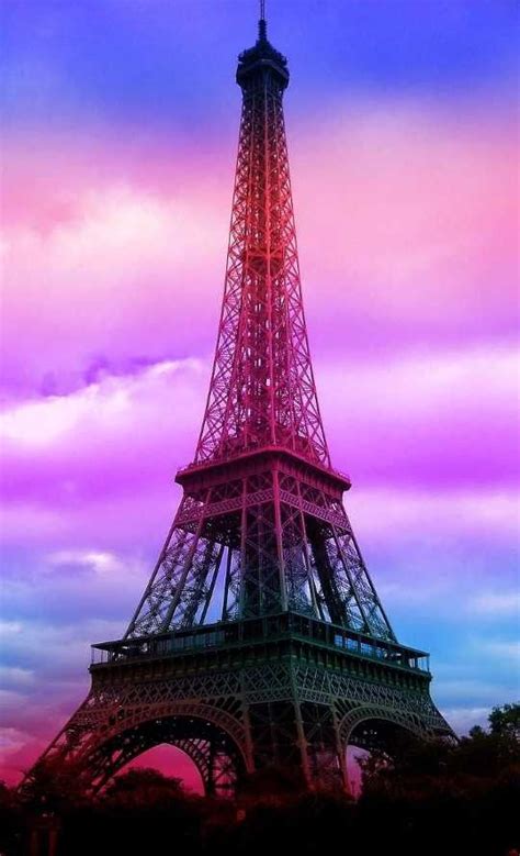 The Eiffel Tower Is Lit Up In Pink And Blue Colors With Clouds Behind It