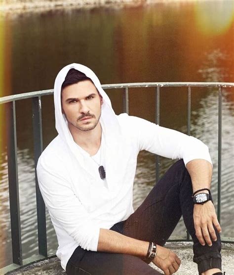 A Man In White Shirt And Black Pants Sitting On Railing Next To Water