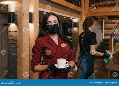 A Female Restaurant Manager Who Wears A Face Mask Is Holding A Cup Of