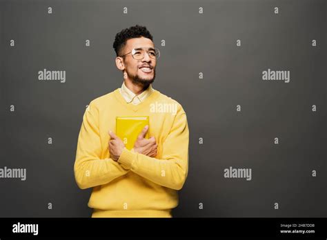 Smiling African American Man In Glasses And Yellow Outfit Holding Book