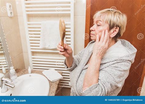 Senior Woman Touching Her Soft Face Skin And Looking In Hand Mirror At