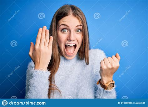 Young Beautiful Redhead Woman Wearing Wedding Ring On Finger Over Blue Background Screaming