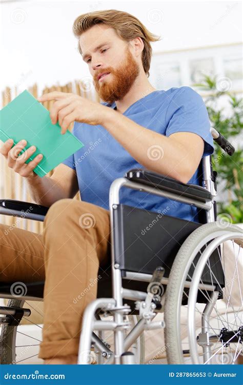 Hombre En Silla De Ruedas Leyendo Libro En Casa Imagen De Archivo