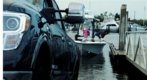 Two People On A Boat In The Water Next To A Dock With Cars And Boats