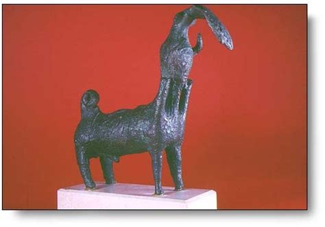 A Bronze Statue Of A Goat On A White Pedestal Against A Red Background