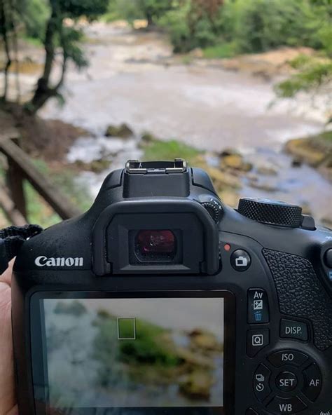 A Person Holding Up A Camera In Front Of A River