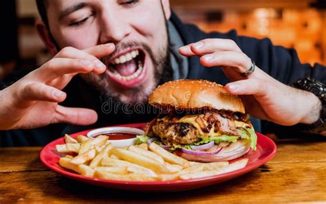 Young Man Eating A Cheeseburger Restaurant Background Stock Image