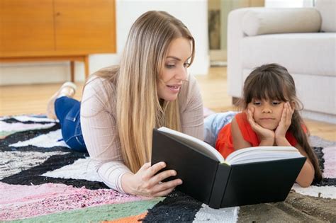 Mère Blonde Allongée Sur Un Tapis Avec Sa Fille Et Son Livre De Lecture