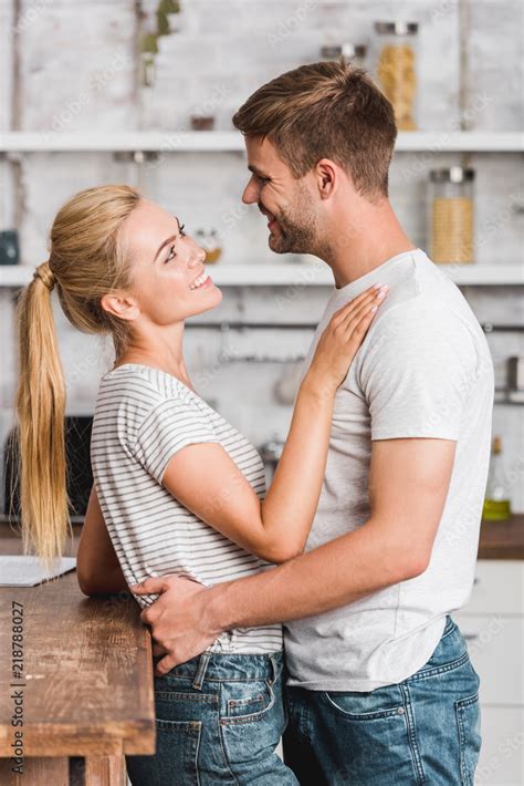 Side View Of Happy Heterosexual Couple Hugging In Kitchen And Leaning