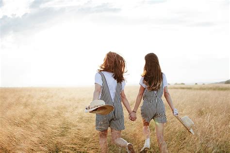 Rear View Of Happy Twin Sisters Holding Hands While Walking On Grassy