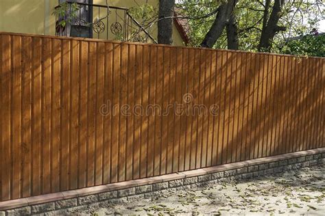 Une Longue Clôture De Bois Brun Devant Une Rangée De Conifères Verts