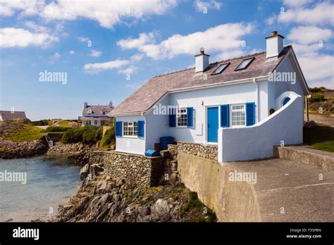 Traditional Welsh White And Blue Cottage Overlooking A Rocky Cove In