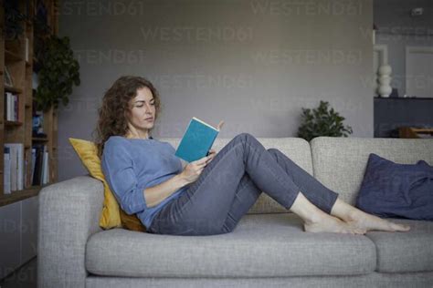 Woman Reading Book While Sitting On Sofa At Home Stock Photo Books To