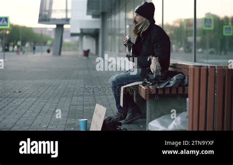 Homeless Young Man Eating Sandwich And Drinking Alcohol From Paper Bag