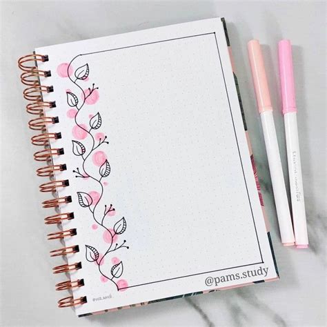 An Open Notebook With Pink Flowers On It And Two Pens Sitting Next To