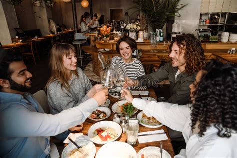 Group Of Smiling Friends Clinking Wine Glasses While Dining In