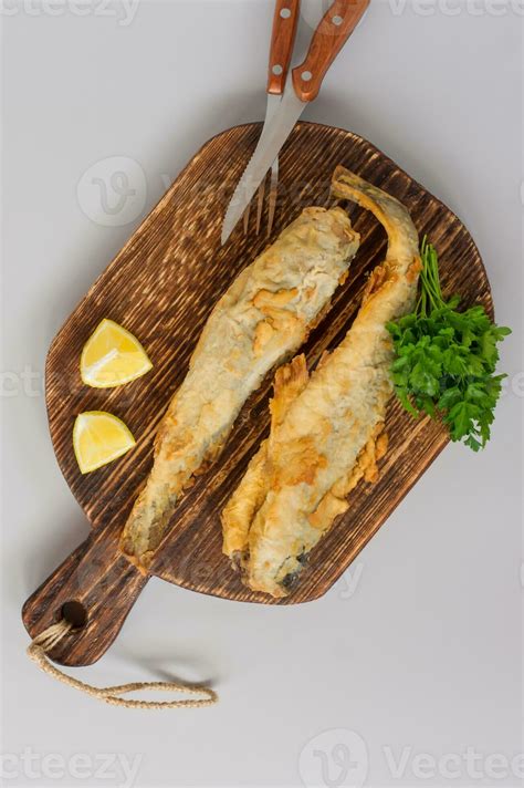 Top View Of Fried Fish Navaga Served On Wooden Cutting Board With Lemon