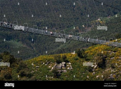 People Walk Across A Narrow Footbridge Suspended Across A River Canyon