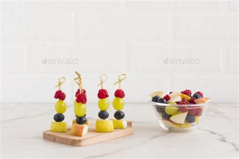 canapes of juicy fruit on a wooden board and a bowl with chopped fruit ...