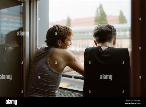 Rear View Of Gay Men Looking Out Of Window In Apartment Stock Photo Alamy