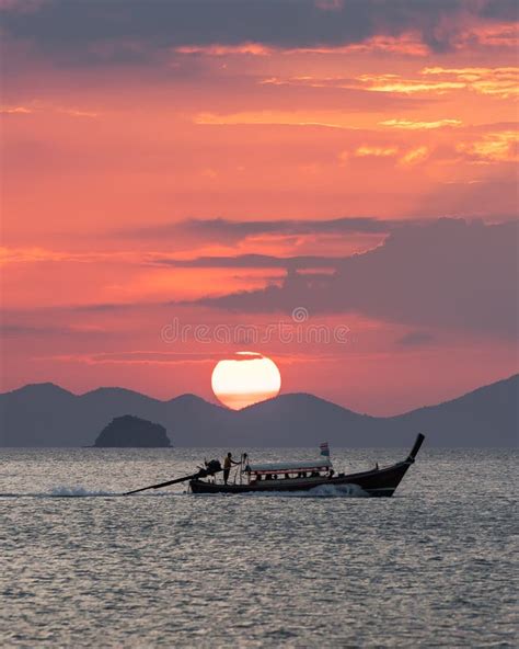 Tthai Longtail Boat In The Sea At Sunset With Big Red Sun And Mountains