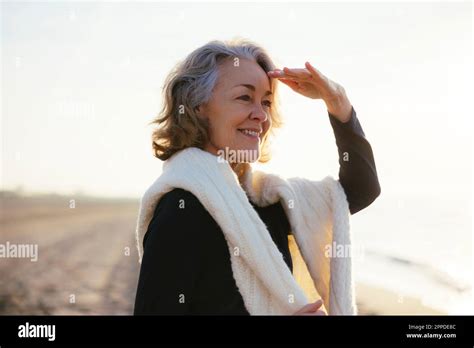 Happy Mature Woman Shielding Eyes Standing At Beach Stock Photo Alamy
