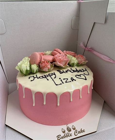 A Pink Birthday Cake With White Icing And Flowers On Top Is In A Box