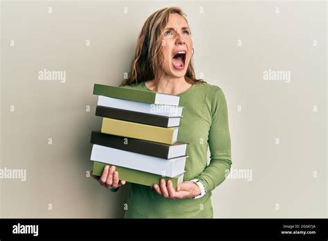 Jeune femme blonde tenant une pile de livres en colère et folle criant frustrée et furieuse