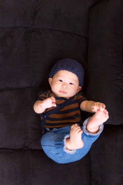 Japanese Baby Lying On Black Sofa Touching His Foot Vertical Shot