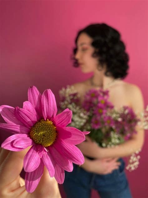 A Woman Holding A Pink Flower In Front Of Her Face