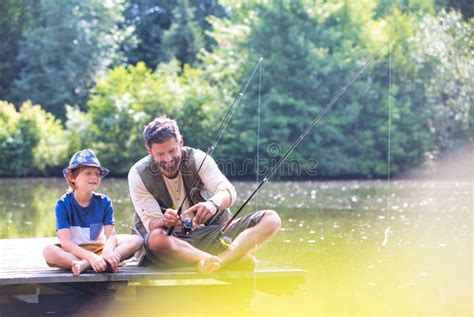 Father And Son Fishing In Lake While Sitting On Pier Stock Image