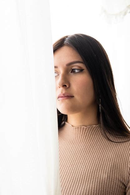 Una mujer adulta joven latina con el pelo largo está mirando por la ventana detrás de una