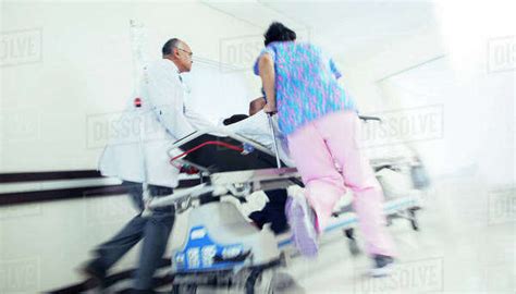 Doctor And Nurse Rushing Patient On Stretcher In Hospital Corridor