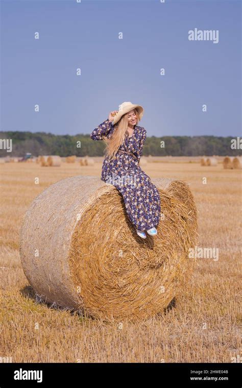 Une jeune fille blonde aux cheveux longs dans un chapeau blanc se repose et pose près des gerbes
