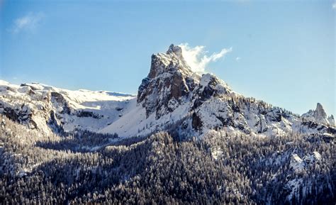 a tall snow capped mountain peak rising above its wooded slopes, tall