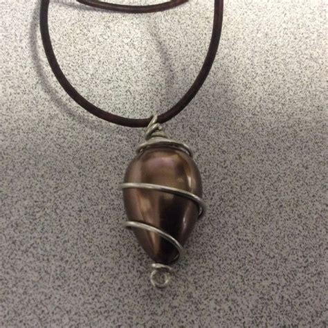 A Necklace With A Heart Shaped Pendant Hanging From Its Side On A Brown Leather Cord