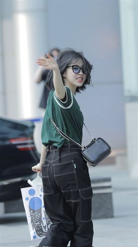 A Woman In Green Shirt And Black Pants Walking Down Street With Hand Up