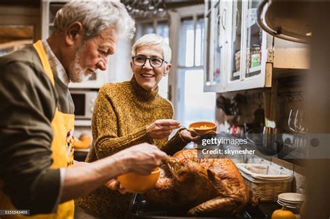 Happy Senior Couple Decorating Turkey On Thanksgiving Day High Res