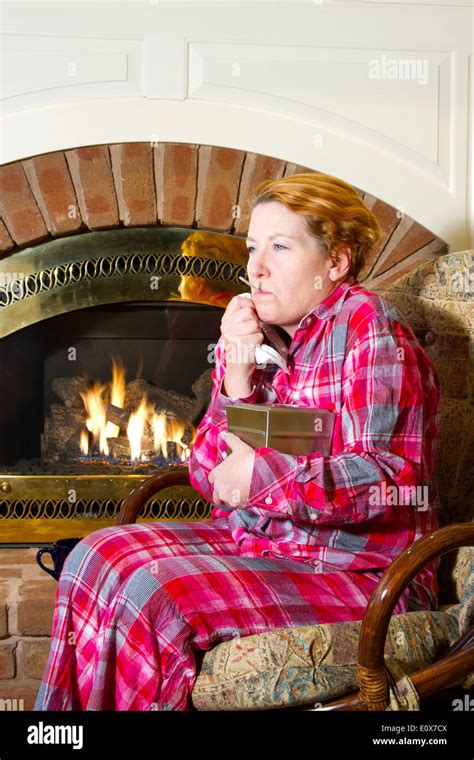 Mature Woman Dressed In Flannel Pajamas Sitting In A Chair In Front Of A Fireplace In The Home